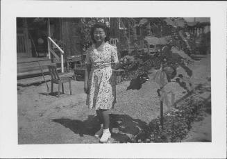 [[Young woman in floral dress next to leafy plant, Rohwer, Arkansas]