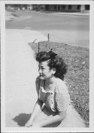 [Young woman in polka dot dress kneeling on sidewalk, Rohwer, Arkansas]