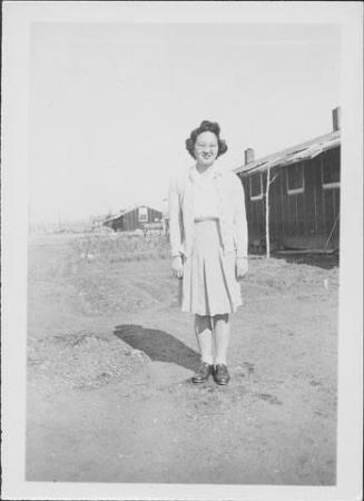 [Sakaye Nakatsuru in sweater and pleated skirt in open area near barracks, Rohwer, Arkansas, January 1944/5?]