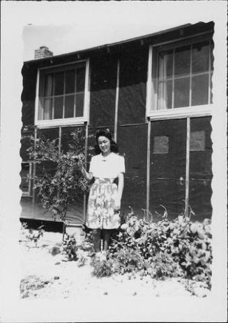 [Young woman standing next to tree in front of barracks, Rohwer, Arkansas]