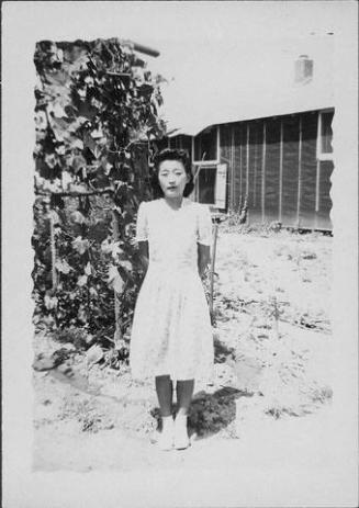 [Woman in spiral patterned dress in front of vines and barracks, full-length portrait, Rohwer, Arkansas, July 9, 1944]