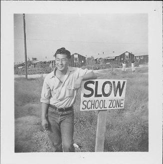 [Smiling man in eyeglasses leaning against "Slow School Zone" sign, Rohwer, Arkansas, October 12, 1944]