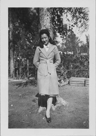 [Young woman in trenchcoat in front of tree, full-length portrait, Rohwer, Arkansas, October 16, 1944]