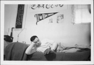[Man reclining on bed reading a magazine below St. Louis Browns pennant, Rohwer, Arakansas, November 9, 1944]