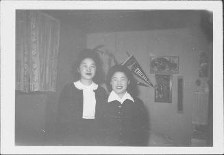 [Two young women standing in room in front of pennants and pictures, Rohwer, Arkansas, January 22, 1945]