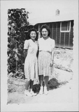 [Two women standing in front of vines and barracks, full-length portrait, Rohwer, Arkansas, July 9, 1944]