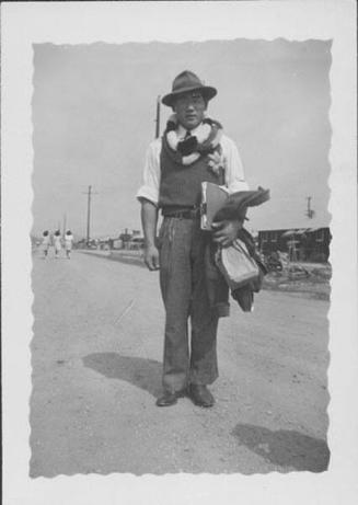 [Man in hat and leis standing on dirt road, Rohwer, Arkansas, 1943]