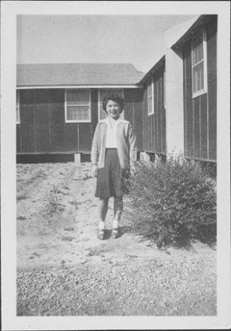 [Young woman standing next to shrub and barracks, Rohwer, Arkansas]