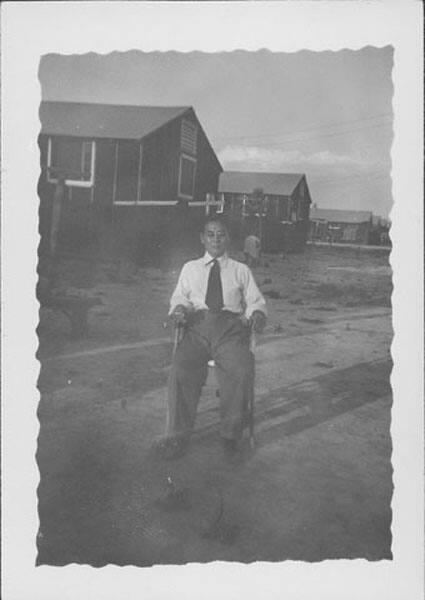 [Man sitting in chair in open area in front of barracks, Rohwer, Arkansas, July 7, 1944]