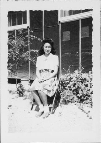 [Young woman sitting on folding chair in front of barracks, Rohwer, Arkansas, August 3, 1944]