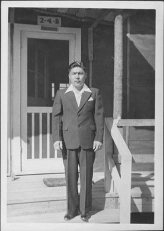 [Man in suit standing on porch steps of barracks, 2-4-B, Rohwer, Arkansas, 1942-1945]