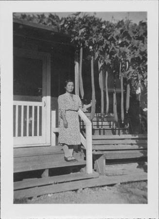 [Woman in patterned dress holding hechima gourd on barracks porch steps, Rohwer, Arkansas]