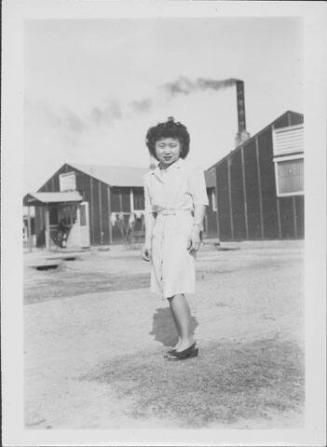 [Young woman in front of mess hall with smoking chimney, full-length portrait, Rohwer, Arkansas, February 28, 1945]