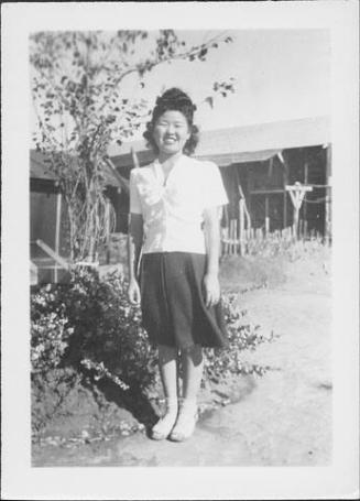 [Young woman standing on path next to tree and shrubs, Rohwer, Arkansas]