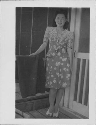 [Young woman in floral patterned suit standing on barracks porch, full-length portrait, Rohwer, Arkansas]