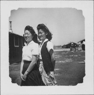 [Two women standing in open area between barracks, three-quarter portrait, Rohwer, Arkansas]