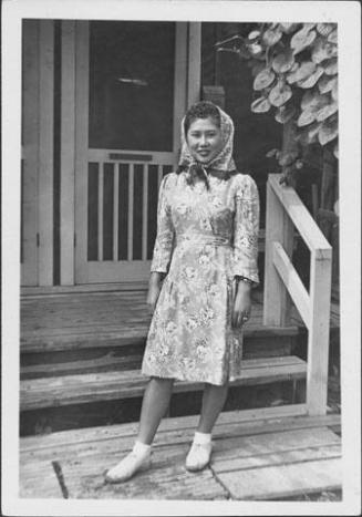 [Young woman in floral dress and headscarf in front of barracks, Rohwer, Arkansas]