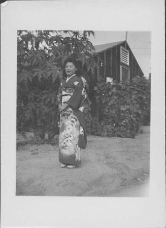 [Young woman in kimono standing in front of tree and barracks, Rohwer, Arkansas]
