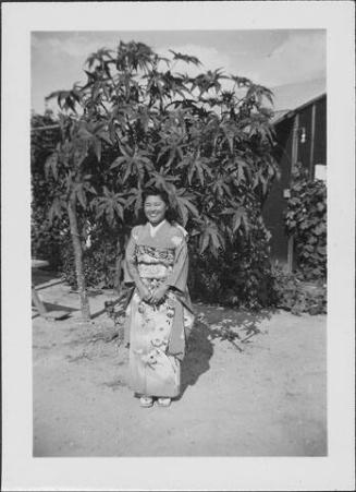 [Young woman in kimono standing in front of tree and barracks, Rohwer, Arkansas]