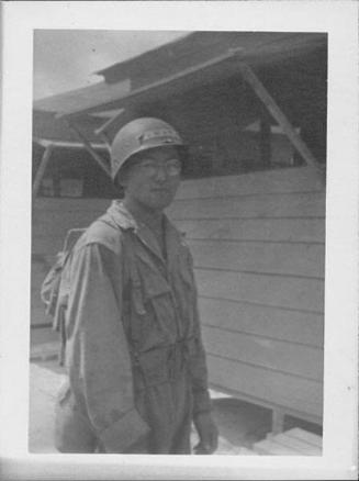 [United States Army soldier in combat uniform and eyeglasses in front of buildings]