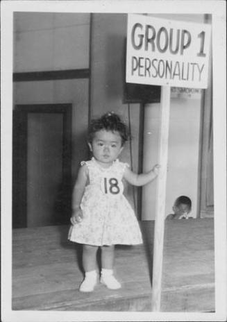 [Toddler in floral dress with sign, "Group 1 personality", Rohwer, Arkansas, July 6, 1944]