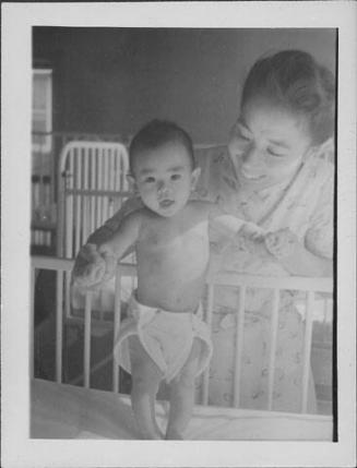 [Infant standing in crib holding woman's hands, Rohwer, Arkansas]