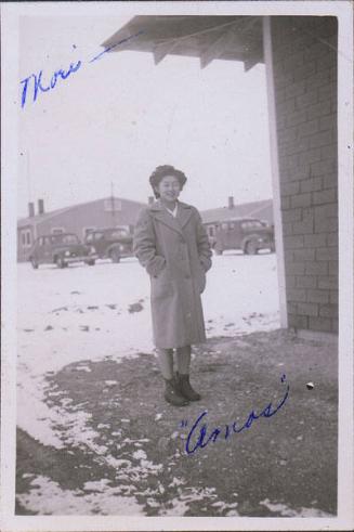 [Portrait of a young woman in overcoat with cars in background, Heart Mountain, Wyoming, Winter 1944-1945]