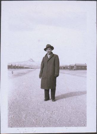 [Portrait of man in hat and coat standing in middle of road with Heart Mountain in background, Wyoming, 1945]