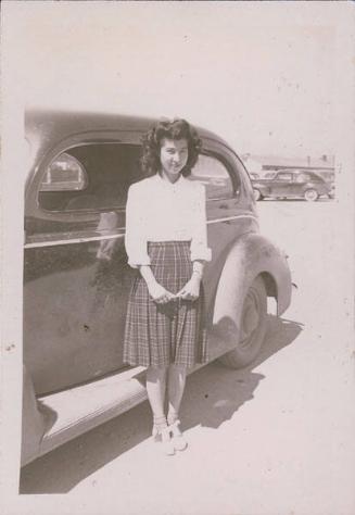 [Young woman in plaid skirt standing in front of car, Heart Mountain, Wyoming, 1942-1945]