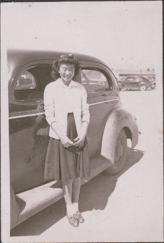 [Young woman with bow in hair standing in front of car, Heart Mountain, Wyoming, ca. 1942-1945]