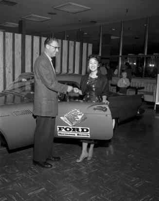 [Caucasian man handing a key to a woman in front of car at Ford Hermosa Beach, California, 1957]