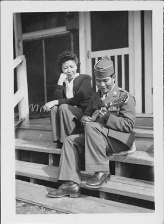 [United States Army soldier playing ukulele next to woman on barrack steps, Rohwer, Arkansas, February 11, 1945]