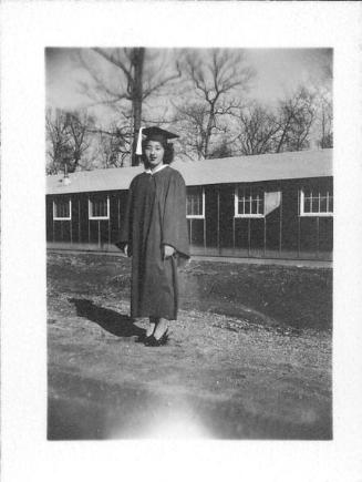 [Young woman in graduation gown and high heels in front of barracks, Rohwer, Arkansas, June 7, 1945]
